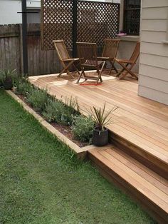 a wooden deck with chairs and plants in the grass next to it on a lawn