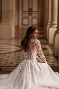 a woman in a white wedding dress sitting on the floor looking off to the side