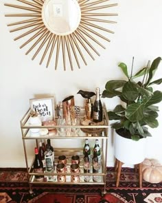 a gold bar cart with bottles on it in front of a wall mounted sunburst