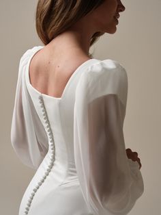 the back of a woman wearing a white dress with long sleeves and buttons on it