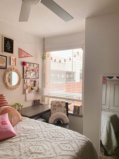 a bedroom with a bed, desk and mirror in it's corner next to a window