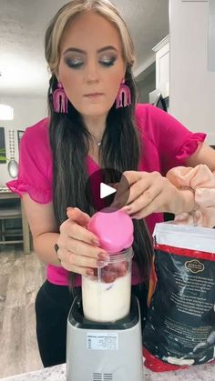 a woman in pink shirt making food on top of a blender with ingredients next to her