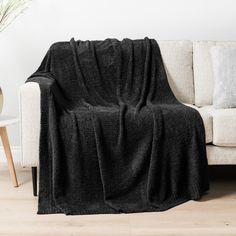 a couch with a black blanket on top of it next to a table and vase