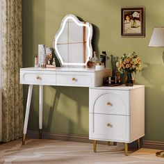 a white dressing table with a mirror and lamp on top of it in front of a green wall