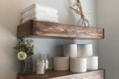 several rolls of toilet paper sitting on top of a wooden shelf next to a vase with flowers