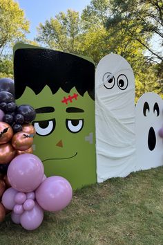 there are balloons and decorations on the grass near some fake ghostes, one is holding a balloon