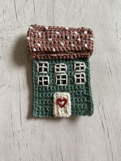 a small crocheted house ornament on a white table with a red heart