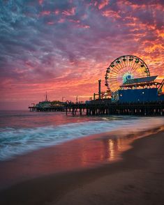 a ferris wheel sitting on top of a sandy beach next to the ocean at sunset