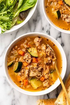 two bowls of soup with meat, vegetables and bread on a marble countertop next to a loaf of bread