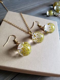 Beautifully elegant yellow flower earrings and necklace set, elegant glass orb earrings with delicate, dried flowers inside. Solid glass ball earrings have warm gold finishing and hooks. Necklace chain is 18 inches in length, and is 18k Gold plated stainless steel. In earlier centuries, a gift of flowers was a meaningful gesture meant to portray the surrounding feelings involved, and show deep affection and appreciation for the receiver. It was known, yellow was worn as a representation of luxur Handmade Gold Glass Jewelry, Dainty Yellow Flower Shaped Jewelry, Yellow Resin Jewelry As A Gift, Yellow Resin Jewelry As Gift, Yellow Resin Jewelry For Gifts, Yellow Resin Jewelry Gift, Glass Drop Earrings For Gift, Clear Flower Shaped Jewelry Gift, Elegant Clear Jewelry With Pressed Flowers