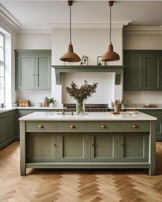 a large kitchen with green cabinets and wooden flooring, two pendant lights above the island