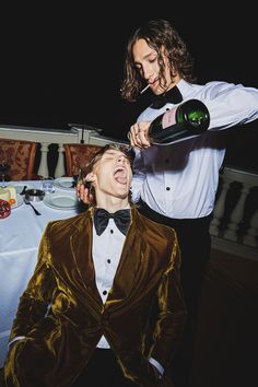 two men in tuxedos are drinking wine