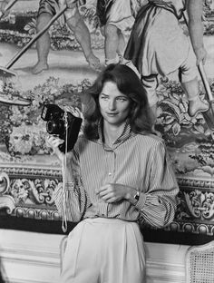 an old photo of a woman holding a camera in front of a wall with paintings on it