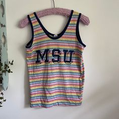 Super cool vintage rainbow striped Michigan State University tank top. Brand is Artex. 100% cotton.  Tagged size medium and measures 17.5 inches pit to pit and 24 inches long. Probably best for a modern small, maybe medium depending on desired fit.  Overall good vintage condition with a tiny mend on the S and a shortened hem  by the previous owner.  Please see last two photos for details. Rainbow Cotton Tops For Spring, Retro Cotton Tank Top For Summer, Striped Rainbow Print Top For Summer, Sleeveless Vertical Stripes Tank Top For Spring, Sleeveless Striped Tank Top For Spring, 90s Style Cotton Vest For Spring, Rainbow Sleeveless Top For Summer, Retro Rainbow Tops For Spring, Colorful Cotton Tops With Rainbow Print