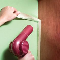 a person using a hair dryer on top of a wooden table next to a green wall