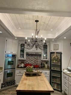 a kitchen with a wooden table in the center and white cabinets on both sides, lights hanging from the ceiling