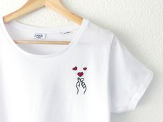 a white t - shirt with red hearts on it hanging from a wooden hanger