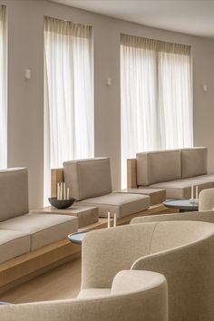 a living room filled with lots of furniture next to two large windows covered in white curtains