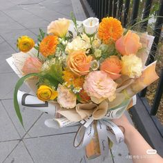 a bouquet of flowers is being held by someone's hand on the sidewalk in front of a fence