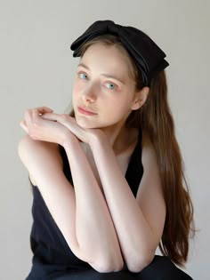 a woman with long hair wearing a black dress and posing for the camera in front of a white wall