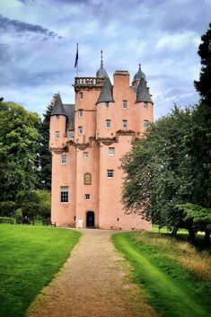 a large pink castle sitting on top of a lush green field under a cloudy sky