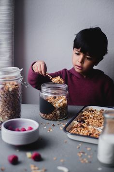 a young boy eating granola from a glass jar on a table next to bowls of cereal