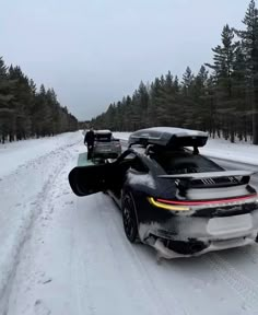 a black sports car driving down a snow covered road with skis on it's roof