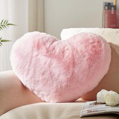 a pink heart shaped pillow sitting on top of a couch next to a white rose