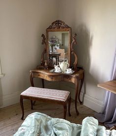 a room with a bed, table and mirror on it's side by the wall