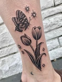 a black and white tattoo on the foot of a woman with flowers, butterflies and stars