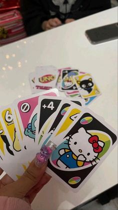 a hand holding four hello kitty playing cards on a table with people in the background