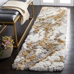 a white and yellow area rug on a wooden floor next to a black bench with a plant in the corner