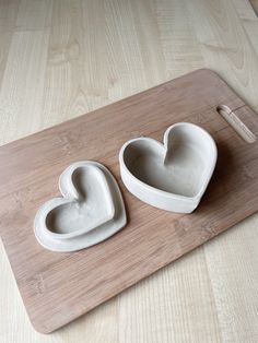 two heart shaped bowls sitting on top of a cutting board