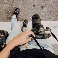 a person sitting on the ground with their legs crossed and holding a camera in one hand