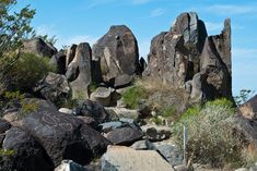 some rocks and bushes on the side of a hill with blue skies in the background