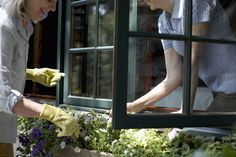 two women in yellow gloves are looking at flowers through a window sill while another woman looks out the window