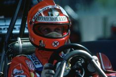 a man sitting in a race car wearing a helmet and holding the steering wheel with both hands