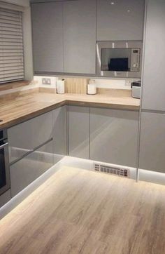 an empty kitchen with grey cabinets and wood flooring on the counter top, along with a microwave oven