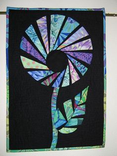 a quilted wall hanging with a flower design on it's side and an abstract background