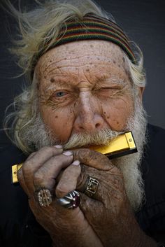 an old man with long white hair holding a gold bar in his mouth