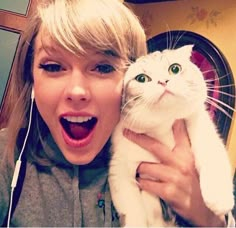 a woman holding a white cat in her arms and making a funny face while wearing headphones