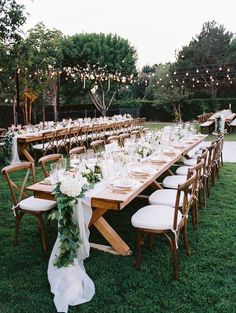 a long table set up with white flowers and greenery for an outdoor wedding reception