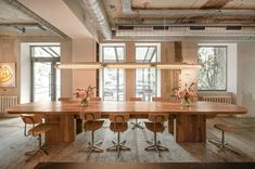 a large wooden table surrounded by chairs in a room with lots of windows and lights