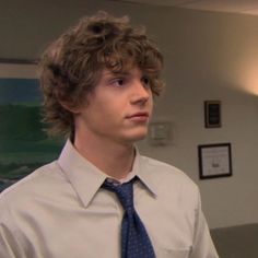 a young man with curly hair wearing a dress shirt and tie in an office setting