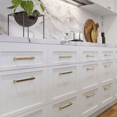 a kitchen with white cabinets and gold pulls on the handles, marble backsplash