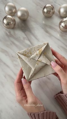 a woman is holding an origami box in her hands and some ornaments on the table