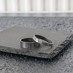 two silver rings sitting on top of a stone slab