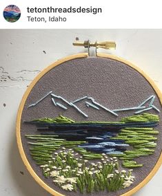 there is a embroidery on the wall with mountains in the background and flowers growing out of it