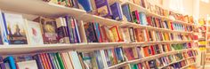 rows of books on white shelves in a room with sunlight coming through the windows and floor to ceiling