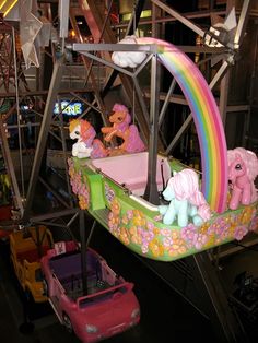 a carnival ride with many ponies and rainbows on the rides, including one pink car